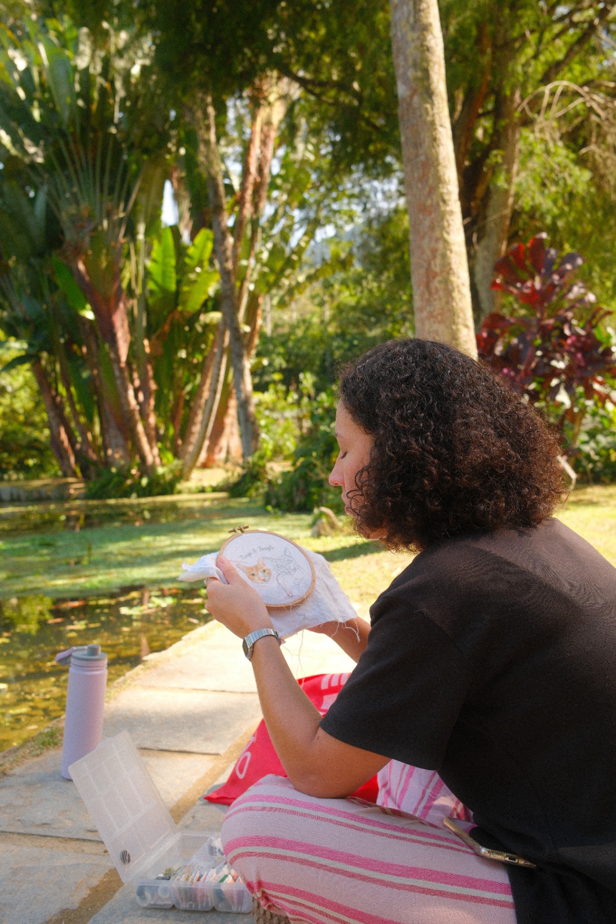 Victória, fundadora do Ateliê do Sentido, bordando com um lago ao fundo